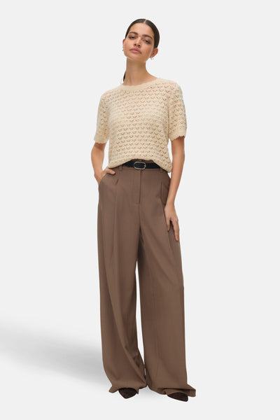 T-shirt beige à manches courtes de VERO MODA, en maille ajourée, porté avec un pantalon marron taille haute.

