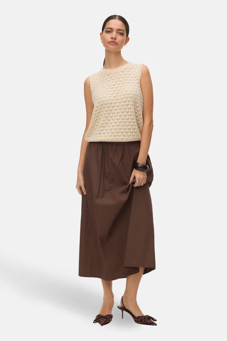 Débardeur écru de VERO MODA® avec motif ajouré, porté avec une jupe marron longue et des escarpins à pois.
