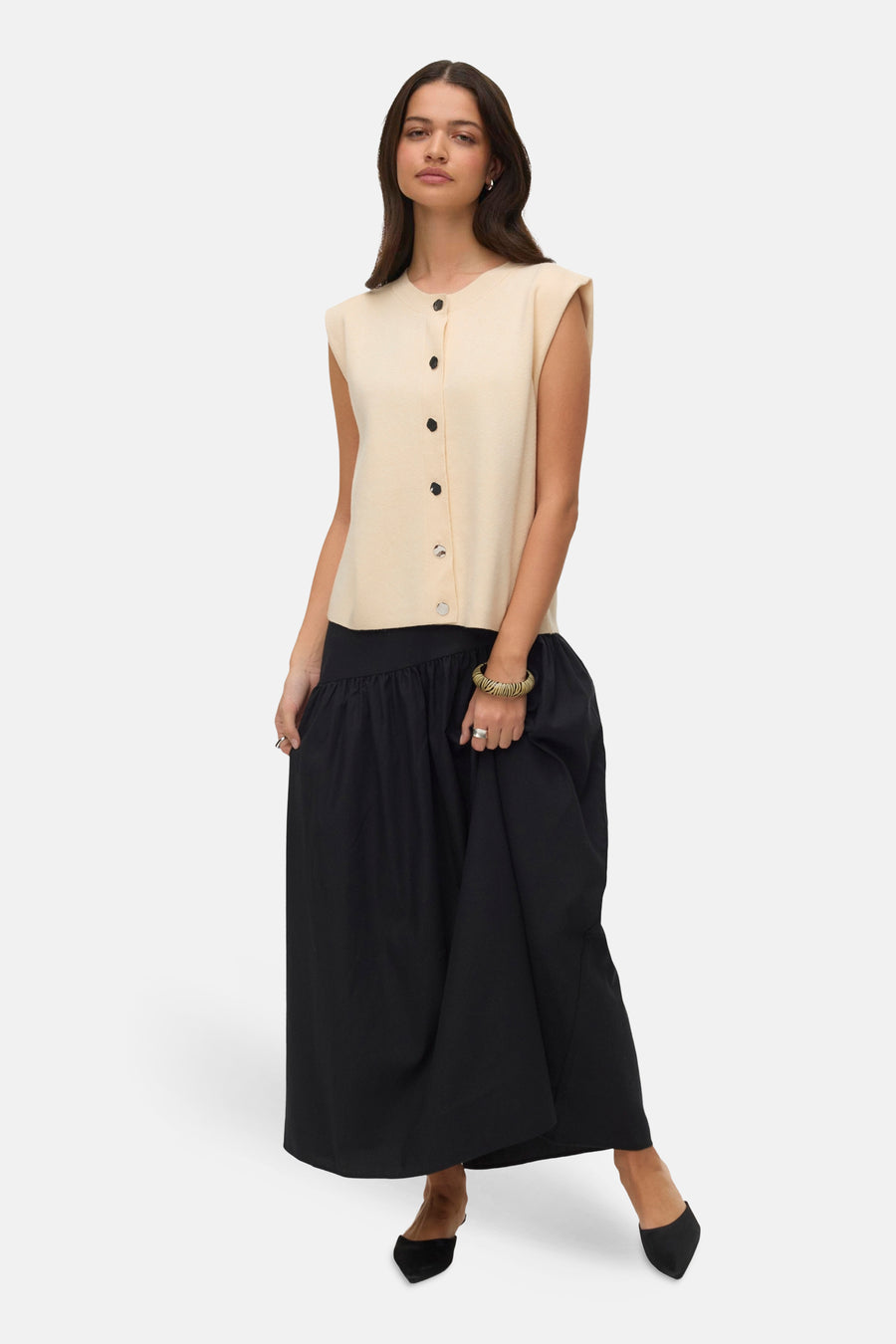 Cardigan écru by VERO MODA, boutonné devant, porté avec une longue jupe noire ample et des escarpins noirs.