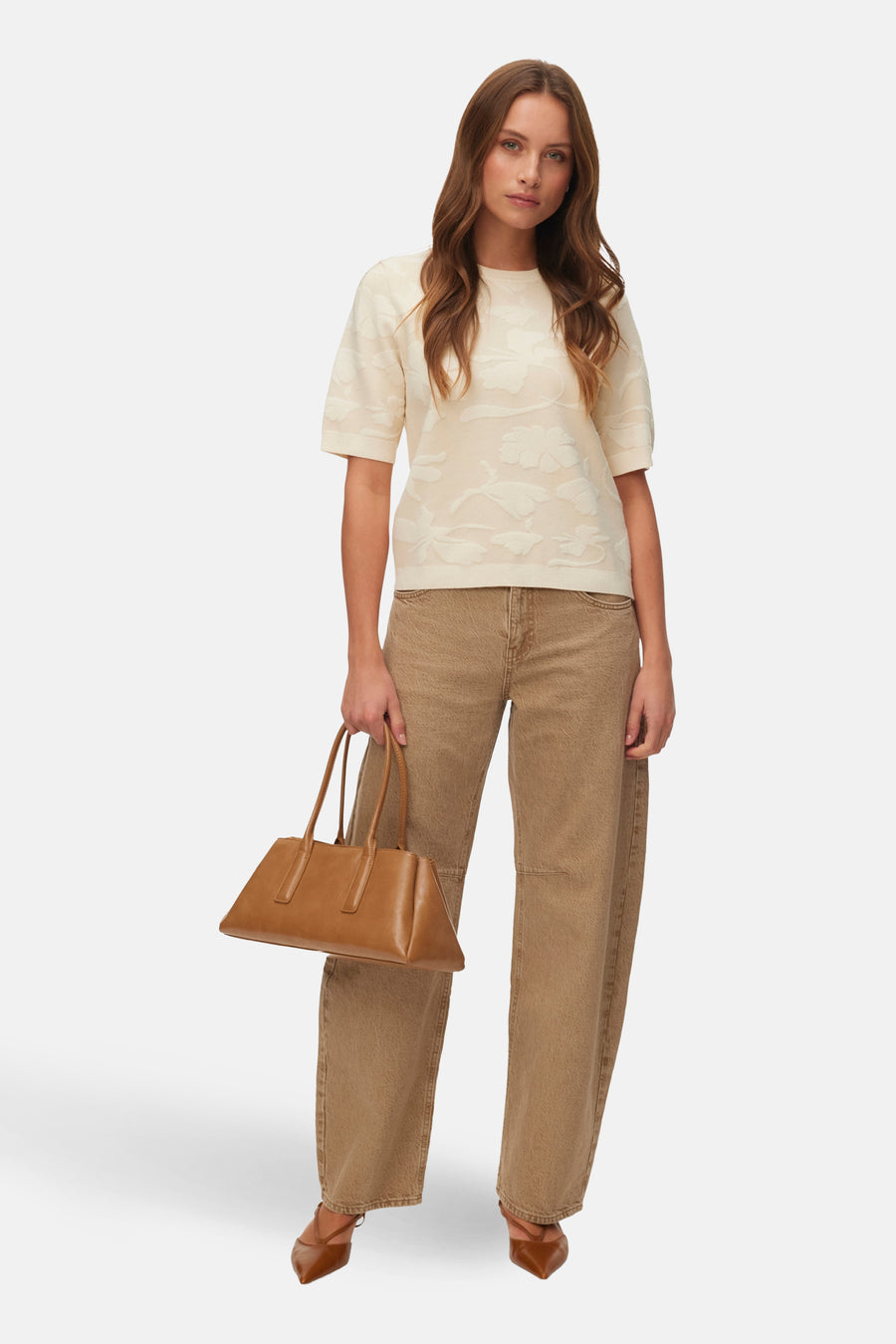 Pull col rond écru de VERO MODA, à motif floral en relief, porté avec un pantalon marron et des escarpins pointus.