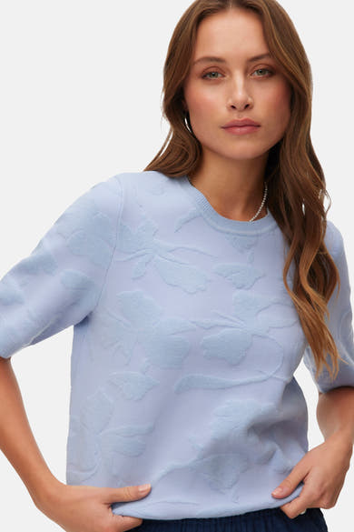 Pull col rond bleu de VERO MODA, avec motif floral en relief et manches courtes.
