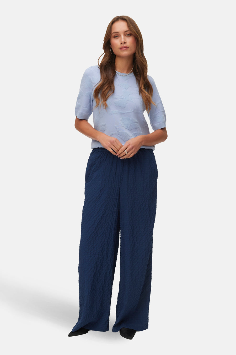 Pull col rond bleu par VERO MODA, à motif floral ton sur ton, porté avec un pantalon ample texturé.
