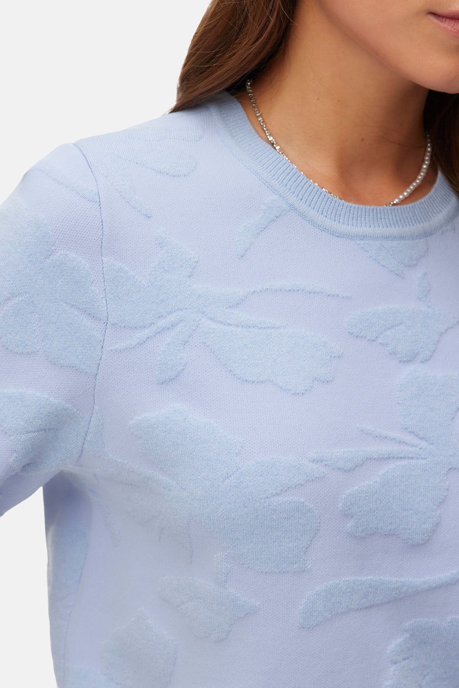 Pull col rond bleu de VERO MODA avec motif floral en relief et collier de perles.
