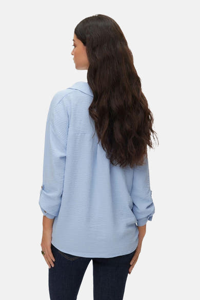 Chemisier à manches longues écru de VERO MODA®, avec des manches retroussées et porté avec un jean.
