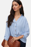 Chemisier bleu à manches longues de VERO MODA®, porté avec une pochette et des bijoux.
