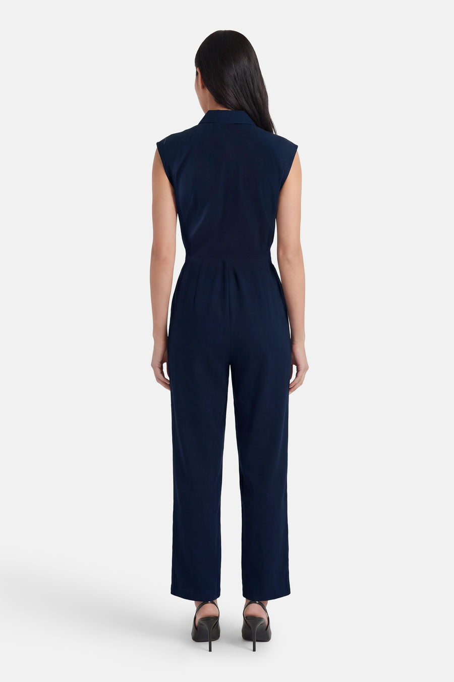 Combinaison bleu marine de VERO MODA®, sans manches, col chemise, taille cintrée, portée de dos avec des escarpins noirs.
