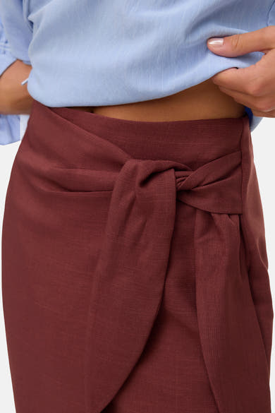 Driekwart rok baksteen van VERO MODA, met strik in de taille, gedragen met een lichtblauw overhemd.