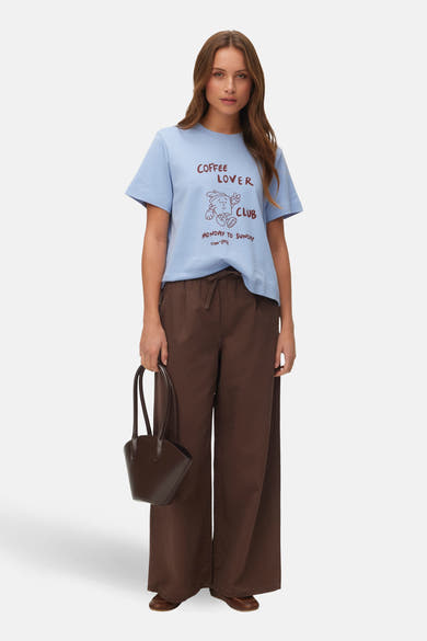 T-shirt bleu à manches courtes de Vero Moda, orné d'un motif « Coffee Lover Club » et porté avec un pantalon marron.