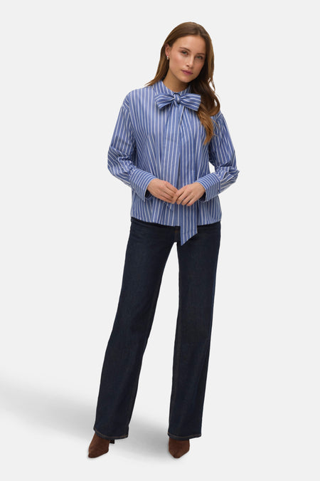 Chemise à manches longues bleue à rayures blanches de VERO MODA, avec un nœud décoratif, portée avec un jean sombre.