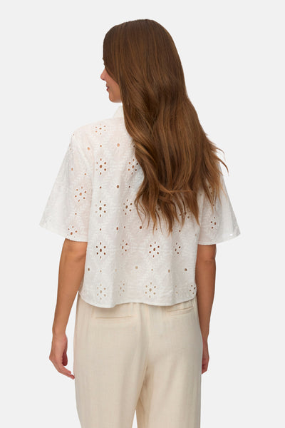 Chemise à manches courtes blanche de VERO MODA avec broderie anglaise florale, vue de dos, portée avec un pantalon beige.