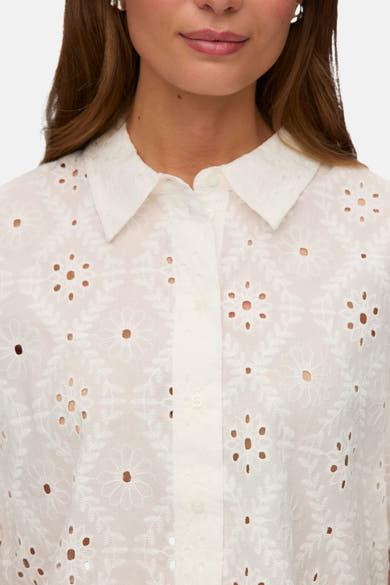 Chemise à manches courtes blanche de VERO MODA® avec broderie anglaise florale, portée par une femme.