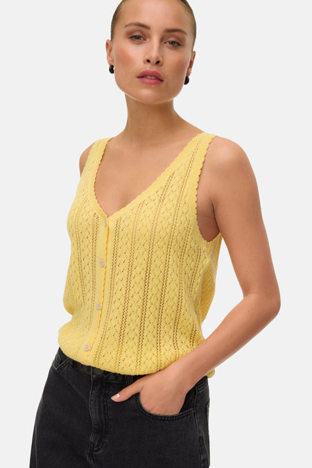 Top sans manches jaune vif de VERO MODA en tricot ajouré, avec col en V et boutons, porté avec un jean noir et des boucles d'oreilles noires.