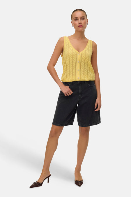 Top sans manches jaune de VERO MODA en maille ajourée à col V boutonné, porté avec un short en jean noir et des mules marron.