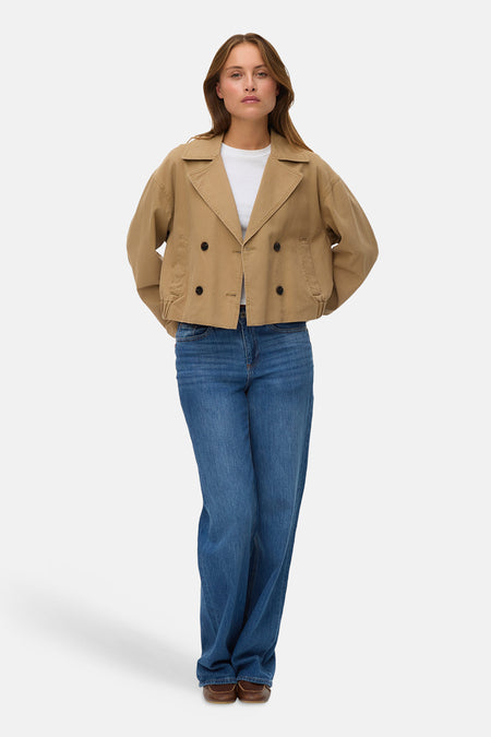 Veste courte brune par VERO MODA®, avec une fermeture à double boutonnage, portée sur un t-shirt blanc et un jean bleu ample.