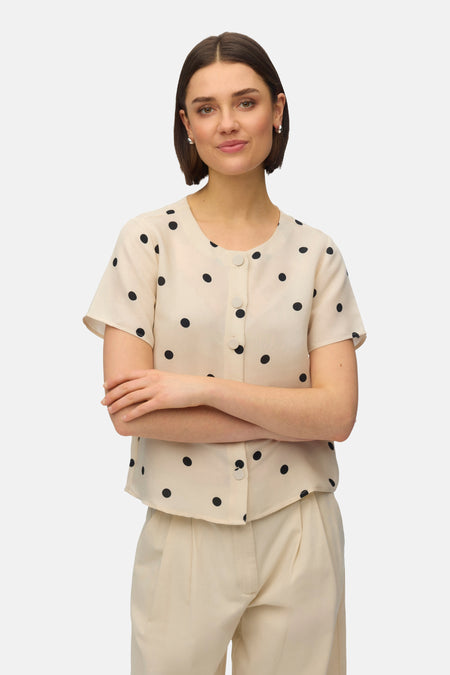 Chemisier à manches courtes multicolore de VERO MODA®, orné de pois noirs, porté avec un pantalon assorti.
