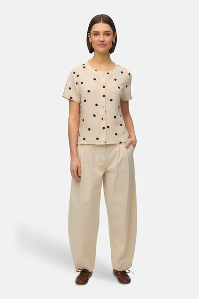 Blouse à manches courtes multicolore de Vero Moda, ornée de pois noirs, portée avec un pantalon beige ample.
