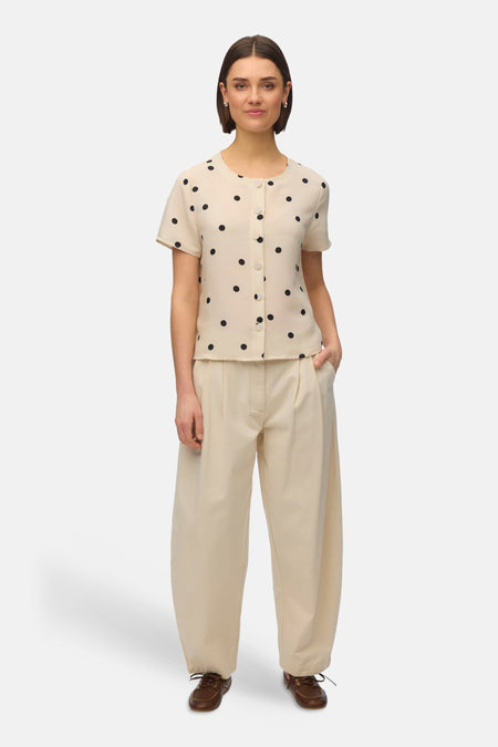 Blouse à manches courtes multicolore de Vero Moda, ornée de pois noirs, portée avec un pantalon beige ample.
