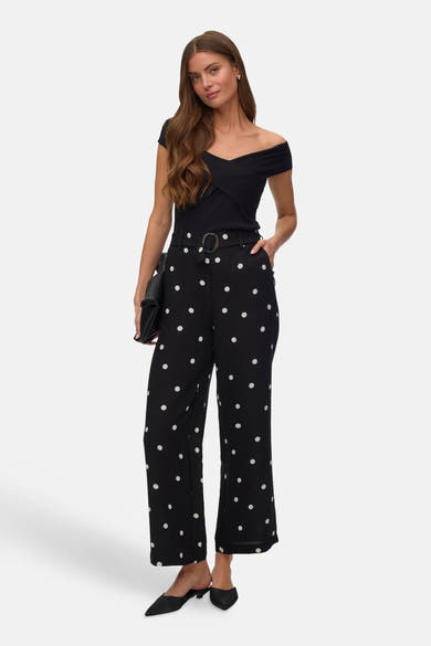 Pantalon noir à pois blancs de Vero Moda, porté avec un haut noir croisé et des mules noires.