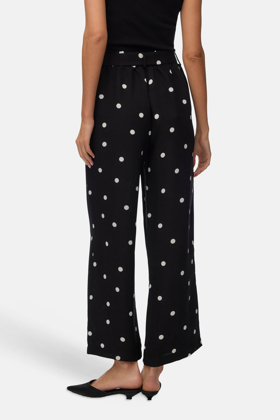 Pantalon noir à pois blancs de Vero Moda, coupe ample et fluide, porté avec des mules noires.

