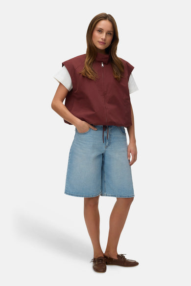 Veste sans manches rouge de VERO MODA, portée avec un t-shirt blanc et un bermuda en jean bleu clair.