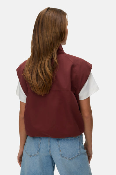 Rood mouwloos vest van VERO MODA, met een opstaande kraag en gedragen met een wit T-shirt en een blauwe jeans.