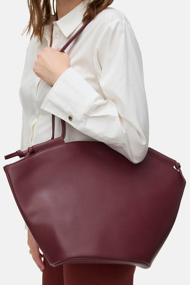 Shoppertas in baksteenkleur van VERO MODA, met een gladde afwerking, met een decoratieve strik, gedragen door een vrouw in een wit overhemd.