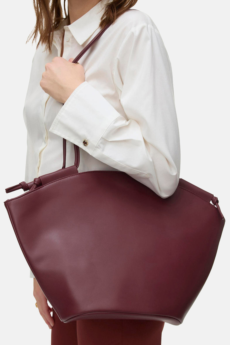 Shoppertas in baksteenkleur van VERO MODA, met een gladde afwerking, met een decoratieve strik, gedragen door een vrouw in een wit overhemd.