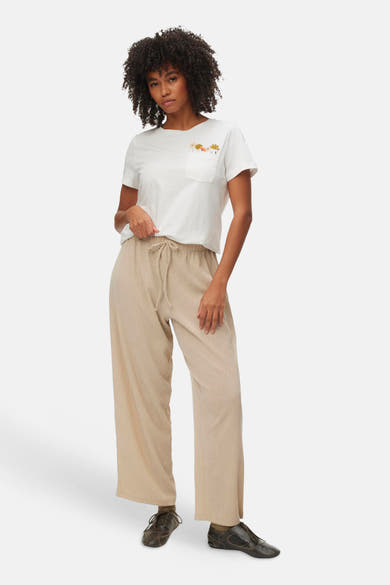 T-shirt blanc à manches courtes de VERO MODA, avec poche poitrine brodée de fleurs, porté avec un pantalon ample beige.