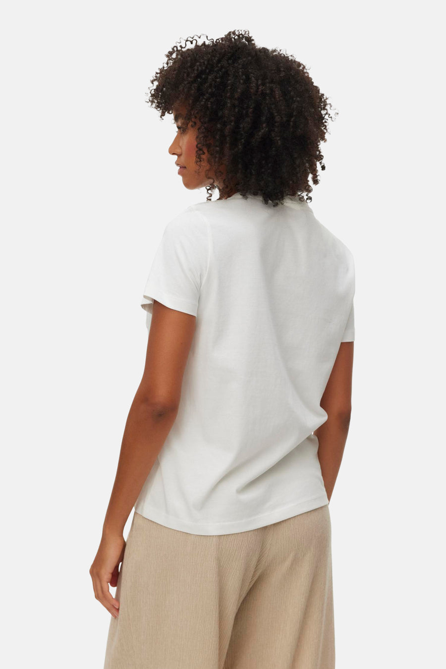 T-shirt blanc de VERO MODA, vue de dos sur une femme aux cheveux bouclés portant un pantalon beige texturé.