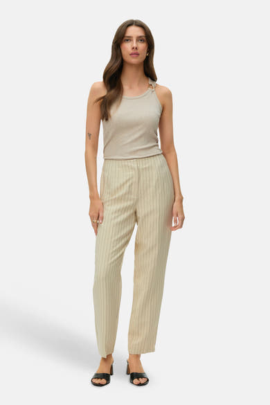 Haut sans manches côtelé beige de VERO MODA® avec anneau doré, porté avec un pantalon rayé et des mules.