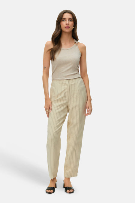 Haut sans manches côtelé beige de VERO MODA® avec anneau doré, porté avec un pantalon rayé et des mules.