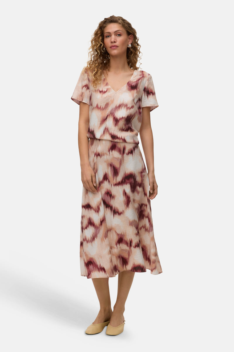 Chemisier multicolore à manches courtes de VERO MODA® avec motif abstrait rose, beige et bordeaux, porté avec une jupe assortie.