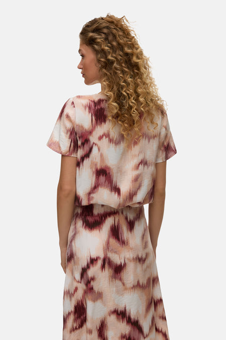 Chemisier multicolore à manches courtes de VERO MODA®, motif abstrait rose et bordeaux, porté par une femme de dos.
