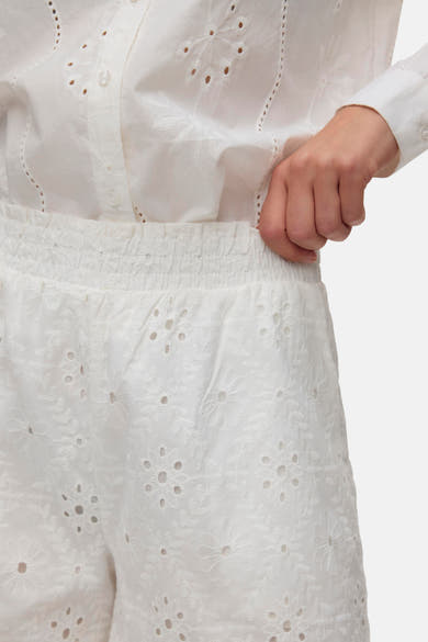 Short blanc de VERO MODA avec broderie anglaise florale et taille élastiquée, porté avec une chemise blanche assortie.