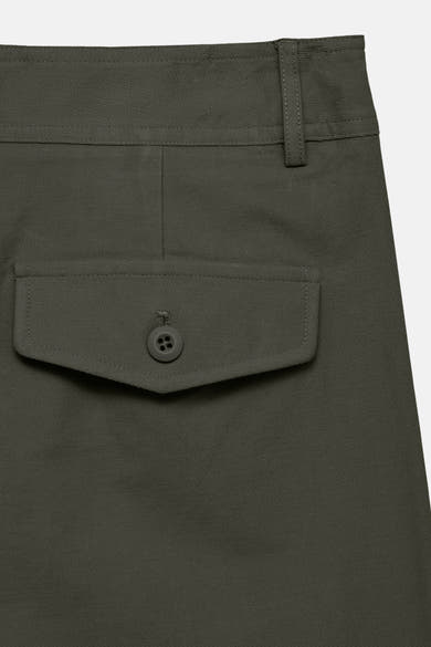 Dark olive colored pants with textured fabric and buttoned flap pocket, close-up side view