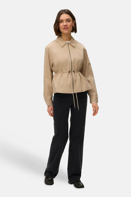 Veste courte beige de VERO MODA, avec cordon de serrage à la taille, portée avec un pantalon noir et des mocassins.