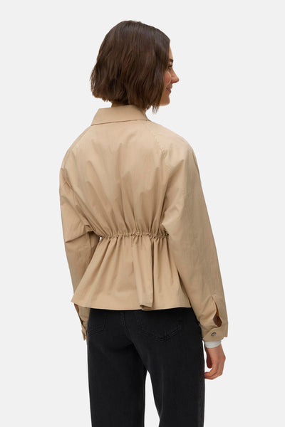 Veste courte beige par VERO MODA avec cordon de serrage à la taille, manches longues et jeans noirs portés.