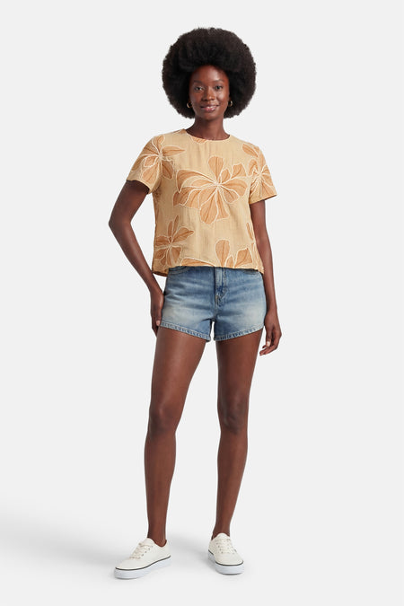 Blouse beige à manches courtes de VERO MODA avec motif floral abstrait marron, portée avec un short en jean et des baskets blanches.