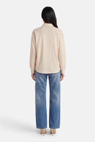 Beige blouse van VERO MODA® met lange mouwen en textuurpatroon, van achteren gedragen met een blauwe jeans en hoge hakken.