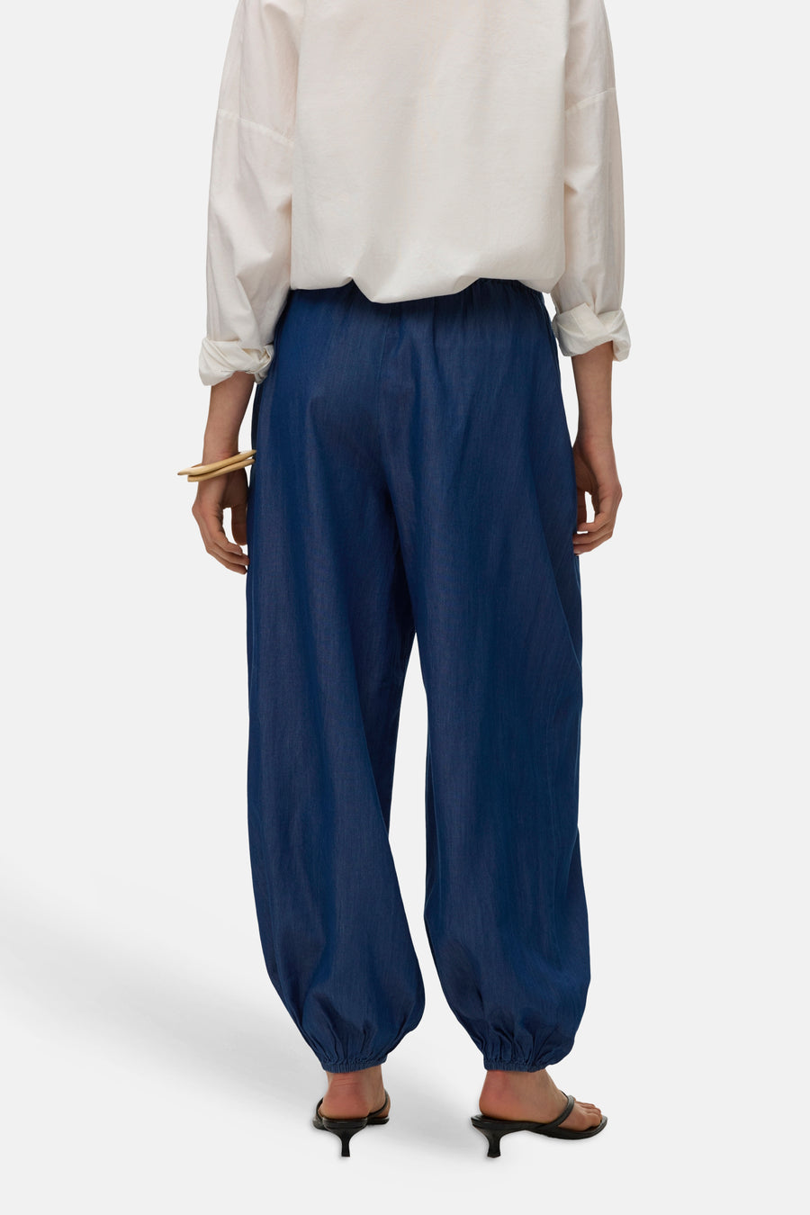 Pantalon ample bleu en denim de VERO MODA, porté avec une chemise blanche et des sandales à talons.
