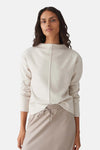 Pull à col rond écru de OPUS, avec couture verticale sur le devant, porté avec un pantalon beige assorti.
