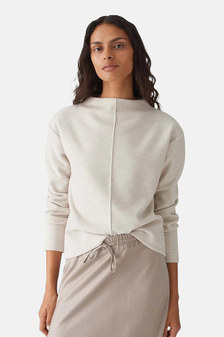 Pull à col rond écru de OPUS, avec couture verticale sur le devant, porté avec un pantalon beige assorti.
