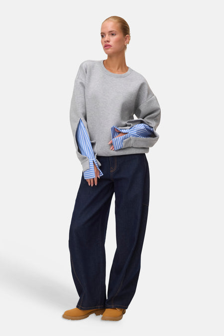 Light grey melange sweatshirt with blue striped sleeve lining, worn with dark denim pants and tan boots, full-length front view