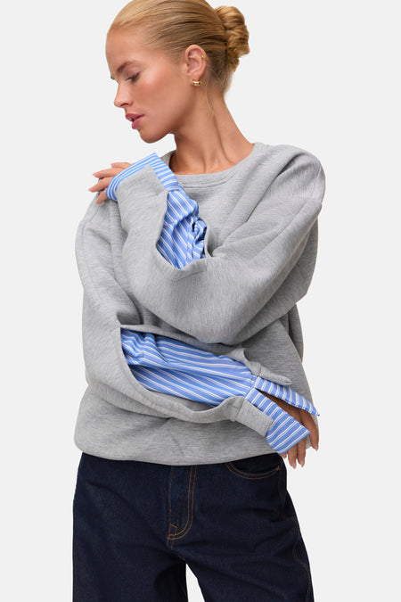 Light grey melange sweatshirt with ribbed cuffs and relaxed fit, worn over blue striped shirt, side view