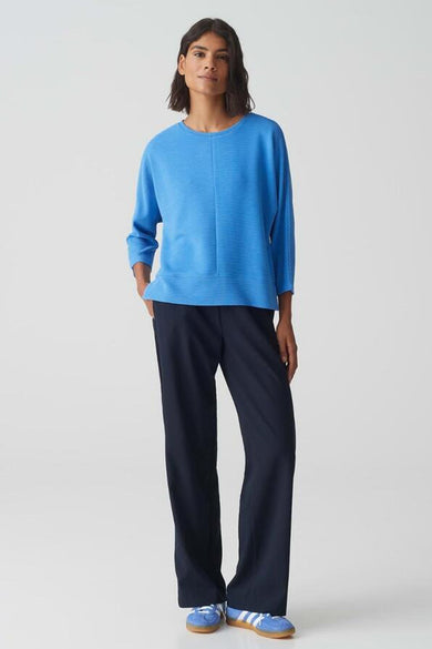Ronde hals trui blauw van OPUS, gedragen met een wijde marineblauwe broek en sportschoenen.