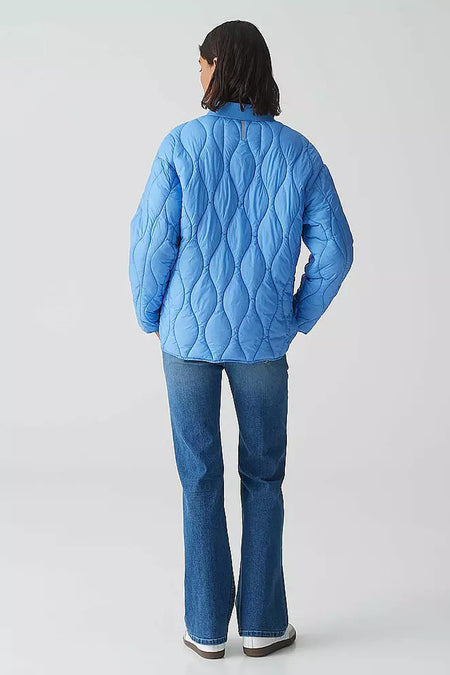 Korte blauwe jas van OPUS, gewatteerd met golvend patroon, gedragen met een blauwe jeans en witte schoenen.