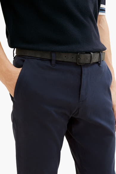 Blauwe chino van Tom Tailor, gedragen met een zwarte riem en een marineblauw gebreid poloshirt.