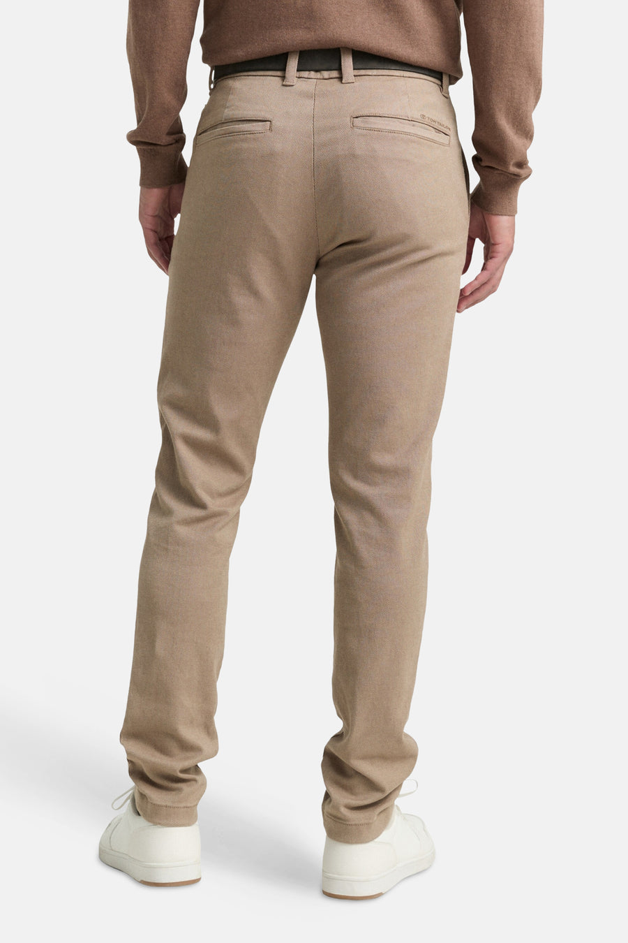 Bruine chino van Tom Tailor, van achteren gezien, met paspelzakken en gedragen met een bruine trui en witte sneakers.