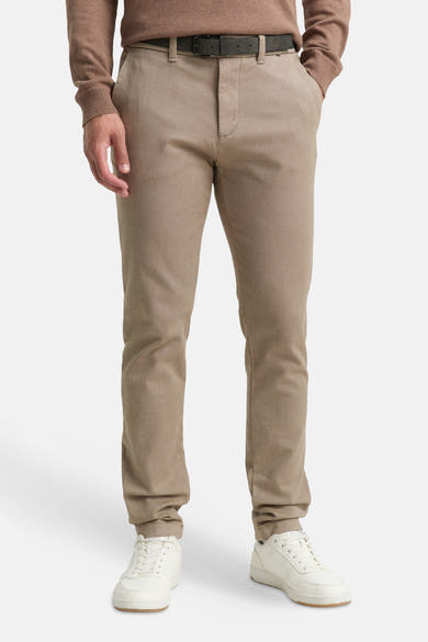Bruine chino, van Tom Tailor, gedragen met een trui in een vergelijkbare kleur, zwarte riem en witte sportschoenen.