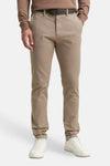 Bruine chino, van Tom Tailor, gedragen met een trui in een vergelijkbare kleur, zwarte riem en witte sportschoenen.